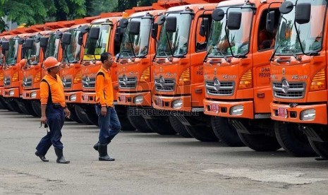 Petugas kebersihan melintas diantara kendaraan truk sampah saat acara peluncuran program peremajaan truk pengangkut sampah di Pulomas, Jakarta Timur, Rabu (11/12).     (Republika/Prayogi)