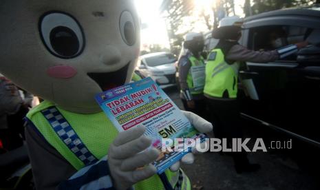 Petugas kepolisian berpakaian badut polisi menunjukkan brosur dilarang mudik saat pengetatan mudik di jalur Pantura, Tegal, Jawa Tengah, Senin (26/4/2021). Pengetatan jalur mudik di jalur Pantura oleh TNI/Polri dan Dinas Perhubungan Kota Tegal dengan memberikan himbauan tentang protokol kesehatan, membagikan masker dan brosur tata tertib lalu lintas tersebut untuk mengantisipasi adanya pemudik awal terkait larangan mudik oleh pemerintah. 