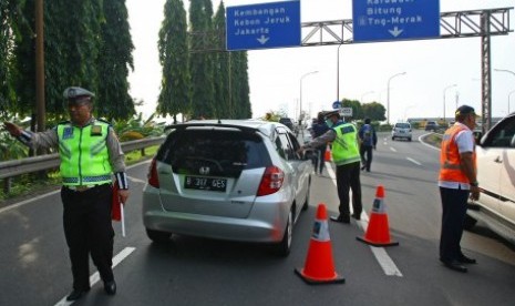 Petugas kepolisian bersama petugas Jasa Marga menghalau pengendara berpelat nomor ganjil yang akan memasuki tol Jakarta-Tangerang (Janger) saat hari pertama uji coba penerapan sistem ganjil genap di Gerbang Tol Tangerang 2, Tangerang, Banten, Senin (16/4). 