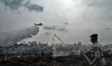 Petugas Kepolisian dibantu pesawat Air Tractor BNPB melakukan pemadaman kebakaran lahan gambut yang terjadi di Desa Rimbo Panjang, Kampar, Riau, Senin (29/8). 