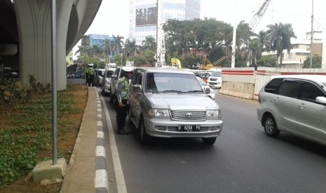 Petugas kepolisian melakukan operasi ganjil-genap di kawasan Pancoran, Jakarta Selatan, Rabu (1/7). Hingga siang hari, telah lebih dari 200 surat tilang dikeluarkan.