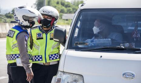 Petugas kepolisian memeriksa identitas dan surat keterangan sehat dari pengemudi kendaraan dengan pelat nomor luar Bandung saat operasi ppkm mikro di gerbang keluar Tol Soreang, Kabupaten Bandung.