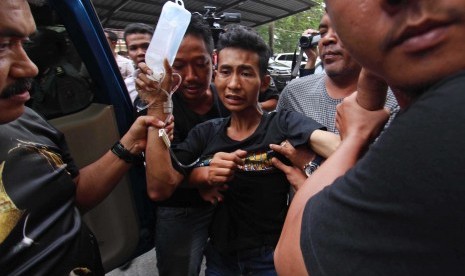 Petugas kepolisian mengiring seorang tersangka bernama Roni (21) yang berhasil ditangkap terkait kasus pembunuhan sekeluarga saat tiba di Mapolda Sumatera Utara, Medan, Rabu (12/4).