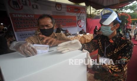 Petugas KPPS mendampingi pemilih yang menggunakan sarung tangan dan masker, memasukan surat suara ke kotak, saat simulasi pemilihan serentak di Padang, Sumatera Barat, Sabtu (21/11/2020). KPU Kota Padang menggelar simulasi dan pemungutan suara serta penggunaan Sirekap di tingkat TPS dalam pemilihan serentak 2020, dengan menerapkan protokol kesehatan COVID-19, di antaranya pemilih harus menggunakan masker, sarung tangan disediakan TPS, membawa pulpen sendiri, dan memilih di bilik khusus jika suhu tubuh di atas 37,3 derajat celcius. 