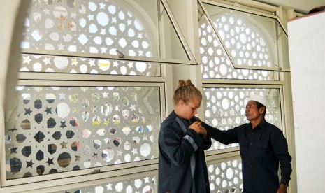 Petugas masjid membantu mengenakan baju khusus penutup aurat kepada wisatawan asing non muslim yang berkunjung di Masjid Raya Baiturrahman, Banda Aceh, Minggu (15/4). 