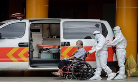 Petugas medis membantu pasien Covid-19 memasuki mobil ambulans.