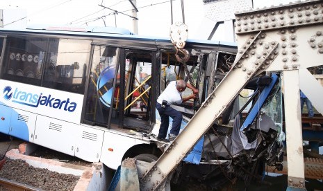 Petugas melakukan evakuasi bus Transjakarta yang mengalami kecelakaan di perlintasan kereta Gunung Sahari, Jakarta Pusat, Kamis (19/5).