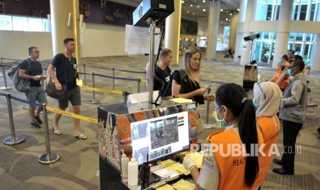 Petugas memantau suhu tubuh penumpang menggunakan alat pemindai suhu tubuh yang dipasang di Terminal Kedatangan Internasional Bandara Internasional I Gusti Ngurah Rai, Bali, Senin (2/3/2020). 