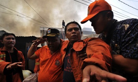  Petugas membantu rekannya yang terluka akibat jatuh dari atap rumah saat berusaha memadamkan kebakaran. (Fanny Octavianus/Antara)