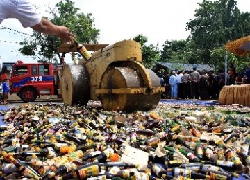 Petugas menggunakan alat berat memusnahkan ribuan botol minuman keras (miras). 