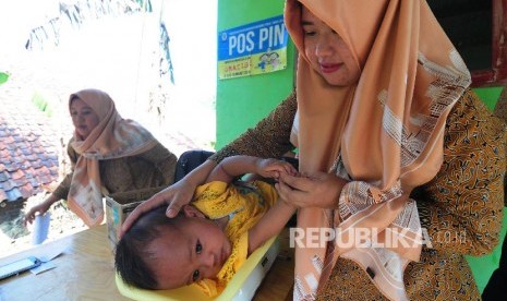 Petugas menimbang berat badan anak-anak di posyandu.