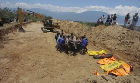 Petugas menurunkan jenazah korban gempa tsunami Palu untuk dimakamkan di Poboya, Mantikulore, Palu, Senin (1/10).