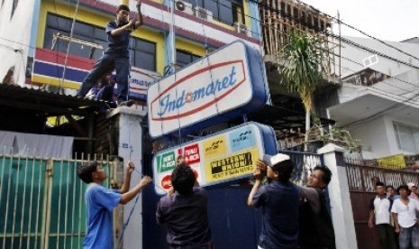 Petugas menurunkan papan reklame saat penertiban minimarket di Indomaret, Jalan Keagungan, Jakarta, Kamis (26/5). 