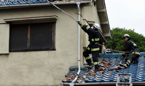 Petugas pemadam kebakaran mencoba menghilangkan puing-puing di atap rumah yang rusak, setelah gempa berkekuatan 6,1 di Osaka, bagian barat Jepang, Senin (18/6) oagi. Gempa bumi ini menewaskan tiga orang dan lebih dari 50 orang terluka. 