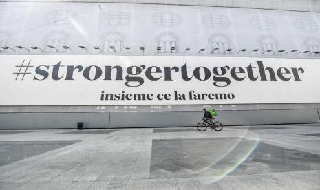  Petugas pengantar makanan melewati spanduk bertuliskan Stronger Together, kita semua akan melewatnya di Milan, Italia, Ahad (5/4). Italia dan beberapa negara Eropa mulai mencatat penurunan kasus Covid-19.