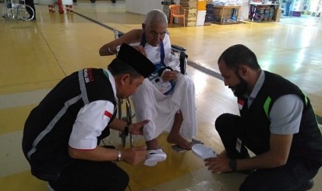 Petugas PPIH Arab Saudi memasangkan sandal untuk Dirah, seorang jamaah asal NTB yang mengklaim berusia 120 tahun di Bandara KAIA Jeddah, Selasa (31/7).