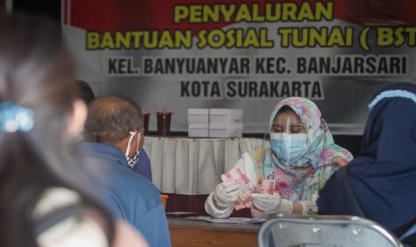 Petugas PT. Pos Indonesia menghitung uang sebelum diserahkan kepada Keluarga Penerima Manfaat (KPM) saat penyaluran Bantuan Sosial Tunai (BST) di Kantor Kelurahan Banyuanyar, Banjarsari, Solo, Jawa Tengah, Senin (26/7/2021). Pemkot Solo mulai menyalurkan bantuan sosial tunai kepada 63 ribu warga Keluarga Penerima Manfaat (KPM) sebesar Rp.600 ribu untuk dua bulan bagi warga yang terdampak COVID-19.