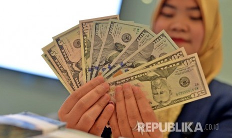 Petugas teller memperlihatkan pecahan uang dolar AS. ilustrasi