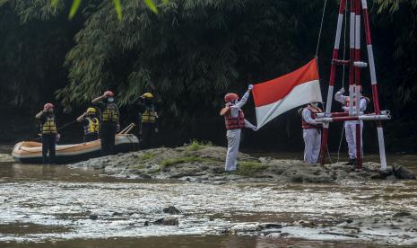 Petugas upacara mengibarkan bendera merah putih saat rangkaian upacara bendera di Sungai Ciliwung, Depok, Jawa Barat, Senin (17/8).