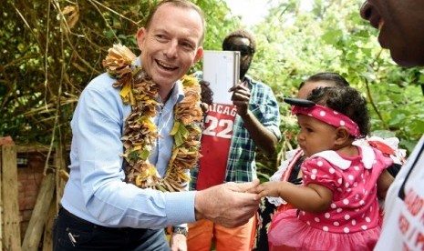 PM Abbott memegang tangan seorang bayi ketika berkunjung ke makam pegiatn pertahanan aborijin Eddie Mabo di Mer Island hari Senin. (AAP: Tracey Nearmy)