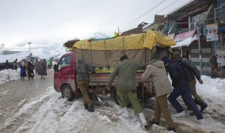 Polisi India mendorong mobil pickup di tengah jalanan bersalju di Desa Kangan, Kashmir, Selasa (14/1).