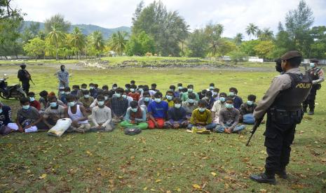 Polisi Indonesia mengawasi sekelompok orang etnis Rohingya setelah mereka mendarat di pantai Indra Patra di desa Ladong, provinsi Aceh, Indonesia, Ahad, 25 Desember 2022. Sebuah perahu kayu yang membawa puluhan Muslim Rohingya mendarat di provinsi paling utara pada hari Ahad. 