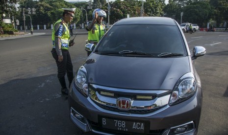 Polisi Lalu Lintas Polda Metro Jaya memberikan imbauan kepada pengendara yang kendaraannya berpelat nomor genap saat uji coba penerapan sistem lalu lintas pelat ganjil-genap di Jalan Medan Merdeka Barat, Jakarta, Rabu (27/7).  