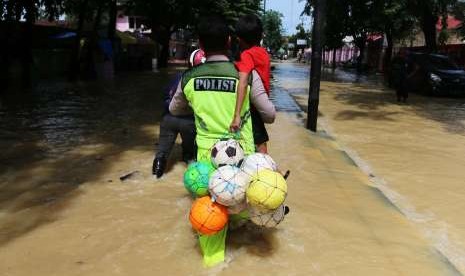 Polisi menggendong seorang anak melintasi banjir di Medan