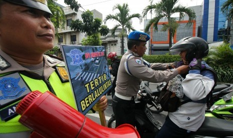 Polisi mengikat tali pengaman helm milik pengendara motor yang tidak terpasang saat Operasi Simpatik (ilustrasi)