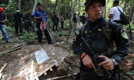 Polisi menjaga kuburan massal di perbatasan Malaysia dan Thailand.