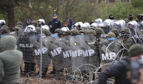 Polisi Polandia dan polisi militer berdiri di belakang pagar perbatasan ketika para migran dari Timur Tengah dan tempat lain berkumpul di perbatasan Belarus-Polandia dekat Grodno, Belarus, Senin, 8 November 2021.