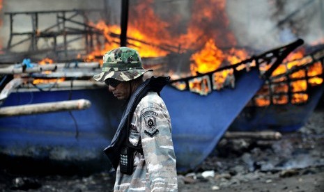 Prajurit TNI AL berjalan di samping kapal penangkap ikan ilegal berbendara negara asing yang dibakar di Pangkalan Angkatan Laut (Lanal) Kota Tahuna, Kepulauan Sangihe, Sulawesi Utara, Kamis (31/12).  (Antara/Stenly Pontolawokang)