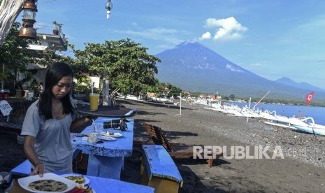 Pramusaji menyiapkan makanan untuk wisatawan saat asap putih terhembus dari kawah Gunung Agung terlihat dari Amed, Karangasem, Bali, Kamis (7/12). 