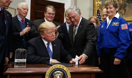 Presiden Donald Trump memegang patung kecil yang diberikan mantan astronot Jack Scmitt (kanan), setelah menandatangani kebijakan mengirim astronot kembali ke Bulan dan Mars, Senin (11/12).