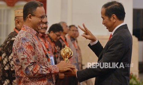 Presiden Joko Widodo (kanan) menyerahkan penghargaan Jaminan Kesehatan Nasional-Kartu Indonesia Sehat (JKN-KIS) Award kepada Gubernur DKI Jakarta Anies Baswedan ketika menerima pengguna manfaat kartu tersebut di Istana Negara, Jakarta, Rabu (23/5). 