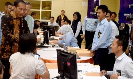 Presiden Joko Widodo (kiri) berbincang dengan petugas pajak saat melayani wajib pajak yang ikut serta dalam program Pengampunan Pajak di Kantor Pelayanan Pajak Gabungan di Jalan M.I. Ridwan Rais, Jakarta, Rabu (28/9).