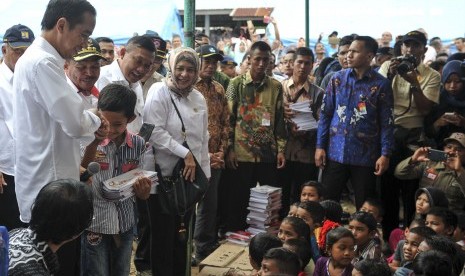 Presiden Joko Widodo (kiri) didampingi Menteri Kesehatan Nila F. Moeloek (kelima kiri) memberikan buku kepada anak-anak korban gempa di halaman Masjid Atta Darut, Pidie Jaya, Aceh, Jumat (9/12).