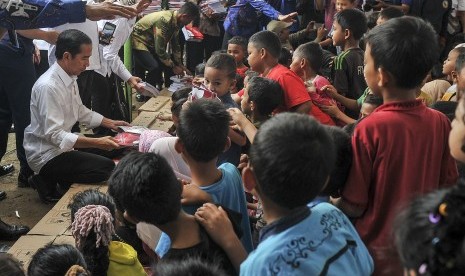 Presiden Joko Widodo (kiri) memberikan buku kepada anak-anak korban gempa di halaman Masjid Atta Darut, Pidie Jaya, Aceh, Jumat (9/12).