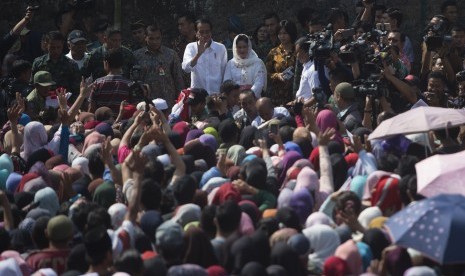 Presiden Joko Widodo (kiri tengah) melambaikan tangan didampingi Ibu Negara Iriana Joko Widodo (kanan tengah) saat membagikan sembako kepada warga di Kampung Caringin, Kabupaten Bogor, Jawa Barat, Rabu (21/6). 