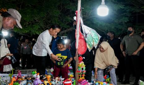 Presiden Joko Widodo membelikan mainan untuk seorang anak saat mengunjungi pasar malam di kawasan Pantai Kamali, Kota Baubau, Sulawesi Tenggara, Senin (26/9/2022). Presiden dalam kunjungannya di wilayah tersebut menyempatkan diri melihat aktivitas pedagang pasar malam dan pelaku UMKM kerajinan lokal. 