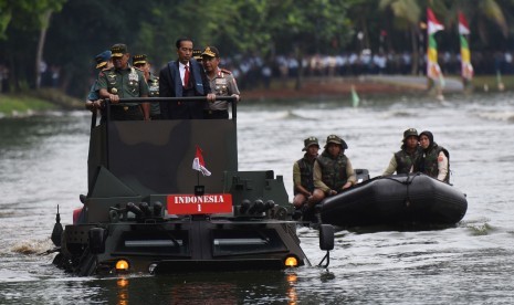 Presiden Joko Widodo (tengah) didampingi Panglima TNI Jenderal TNI Gatot Nurmantyo (kiri) dan Kapolri Jenderal Pol Tito Karnavian (kanan) menyeberangi danau menggunakan kendaraan Panser Anoa 2 6x6 Amphibious sebelum memimpin rapat pimpinan TNI di Mabes TNI