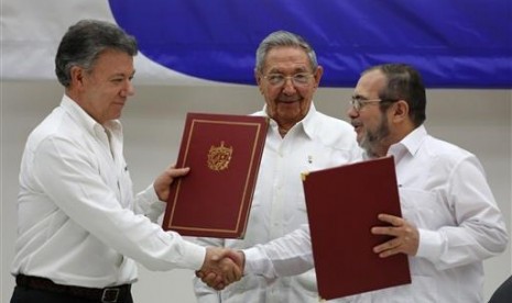 Presiden Kolombia Juan Manuel Santos (kiri) dan Komandan Pasukan Bersenjata Revolusi Kolombia (FARC) Timoleon Jimenez (kanan) berjabat tangan saat menandatangani perjanjian damai di Havana, Kuba, Kamis, 23 Juni 2016. Di tengah adalah Presiden Kuba Raul Cas