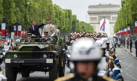 Presiden Prancis Emmanuel Macron memberi isyarat di mobil komandonya di sebelah Kepala Staf Angkatan Darat Prancis Jenderal Francois Lecointre ketika mereka meninjau pasukan sebelum dimulainya parade Hari Bastille di jalan Champs-Elysees di Paris, Ahad (14/7).