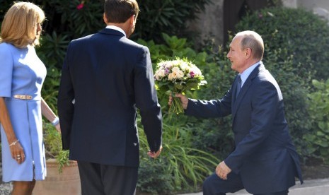 Presiden Rusia Vladimir Putin (kanan) membawa sebuah buket bunga mawar untuk Ibu Negara Prancis Brigitte Macron di Benteng Fort de Bregancon di Bormes-les-Mimosas, selatan Prancis, Senin (19/8). Tampak Presiden Prancis Emmanuel Macron menghadap belakang.