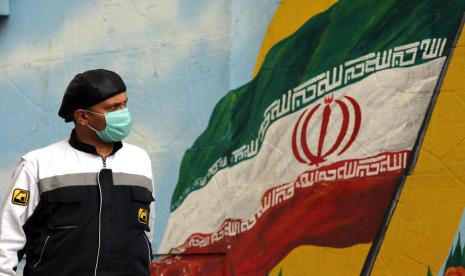 Pria berjalan dengan latar mural bendera Iran.  