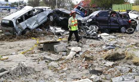 Pria berjalan di puing-puing mobil yang rusak akibat gempa dan tsunami di Kota Palu, Sulteng, Kamis (4/10).