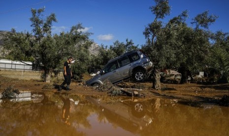 Pria melewati kendaraan yang rusak akibat badai hujan penyebab banjir di Desa Kineta, 68 km dari Athena, Yunani, Senin (25/11).