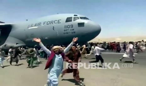  Ratusan orang berlari di samping pesawat angkut C-17 Angkatan Udara AS saat bergerak di landasan bandara internasional, di Kabul, Afghanistan, Senin, 16 Agustus. 2021. 