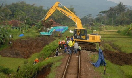 Pekerja menggunakan alat berat memadatkan kembali tanah longsor di perlintasan rel kereta api yang terkena longsor (ilustrasi) 