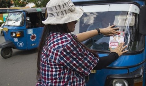 Relawan menempelkan stiker bergambar pasangan capres cawapres Jokowi - Jusuf Kalla 